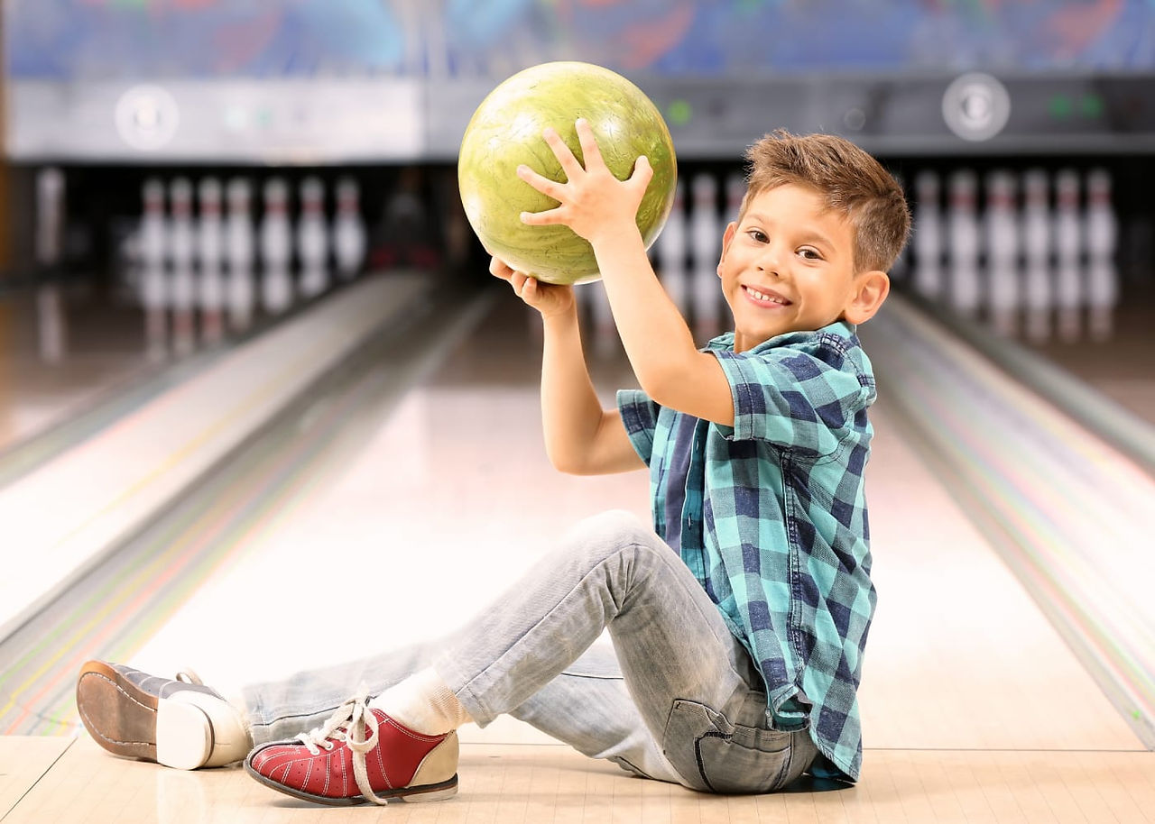 little boy holding bowling ball in front of bowling lane 